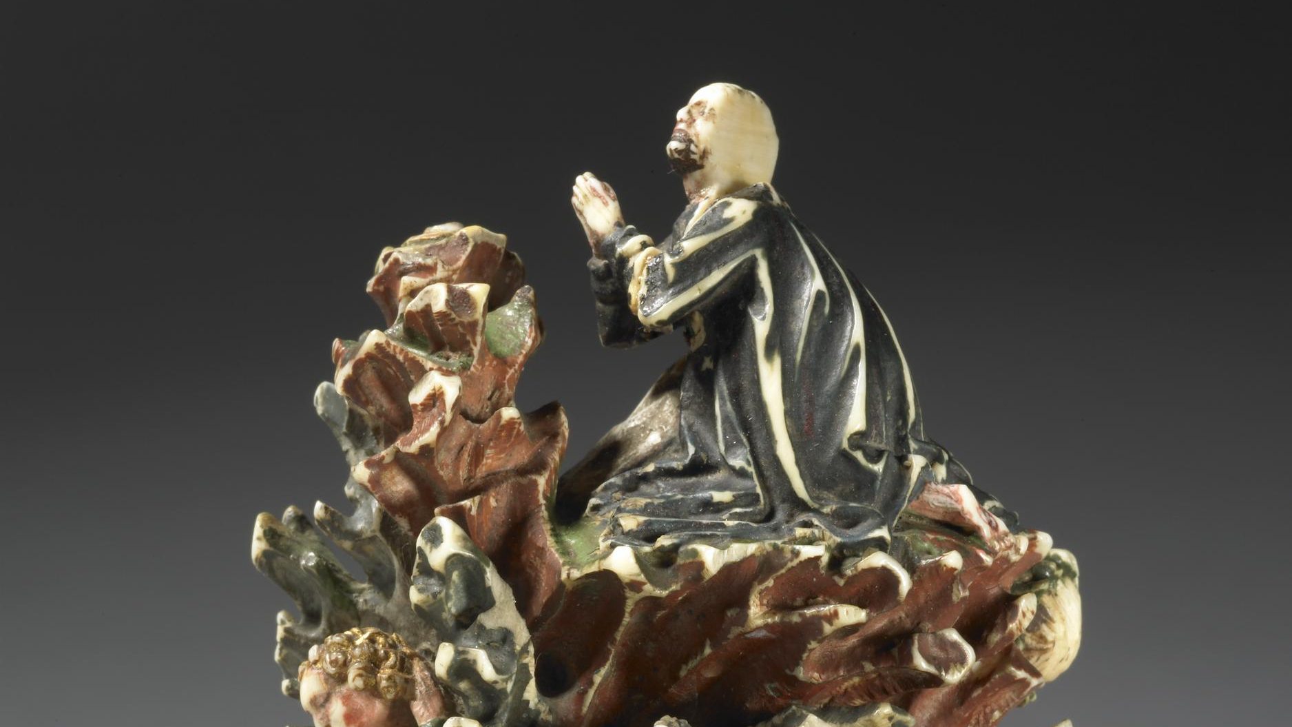 glazed sculture depicting Jesus praying in the garden of Gethsemane. seated sleeping disciples sit beneath him.