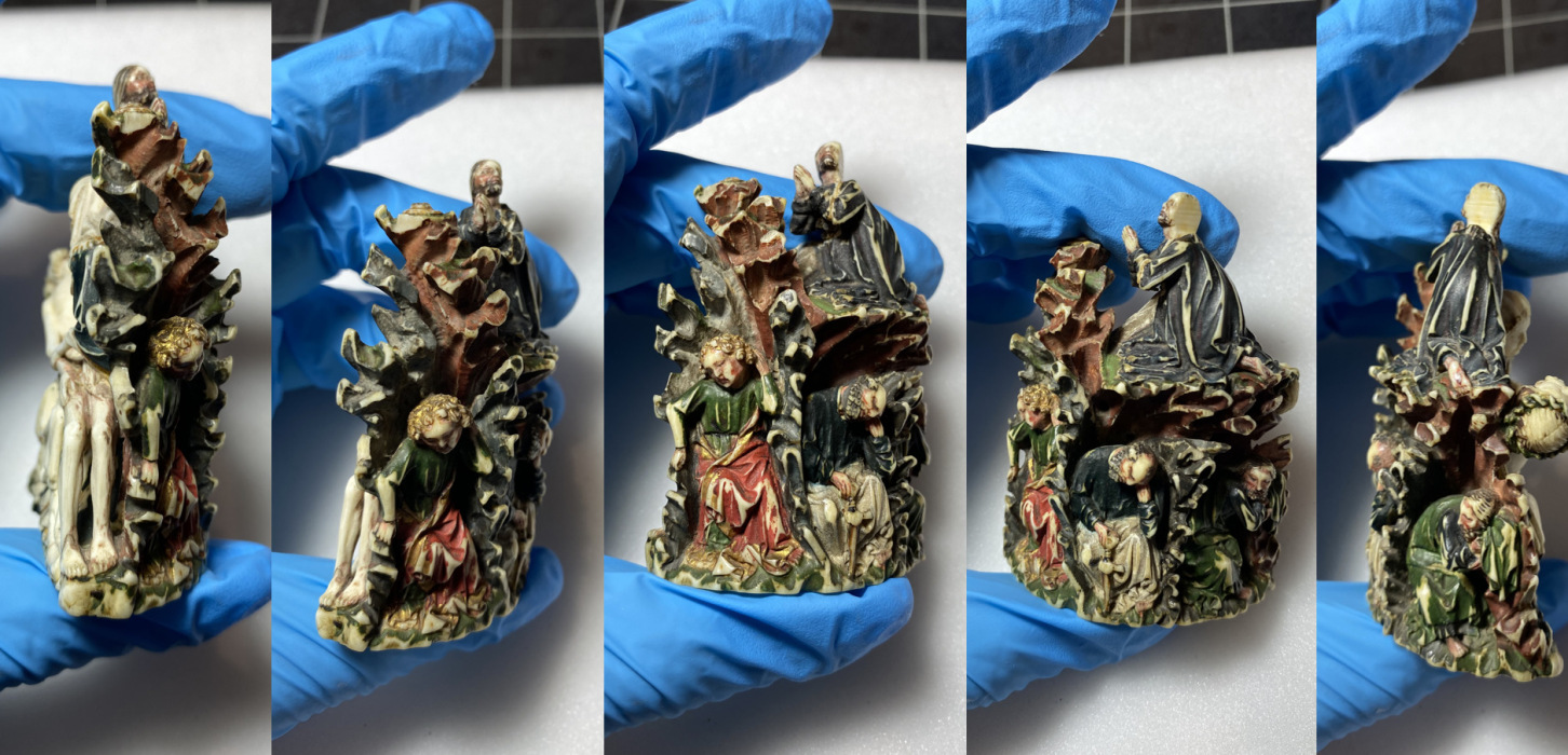 a hand wearing blue gloves holds a small piece of sculpted ivory with polychromy and gilding.