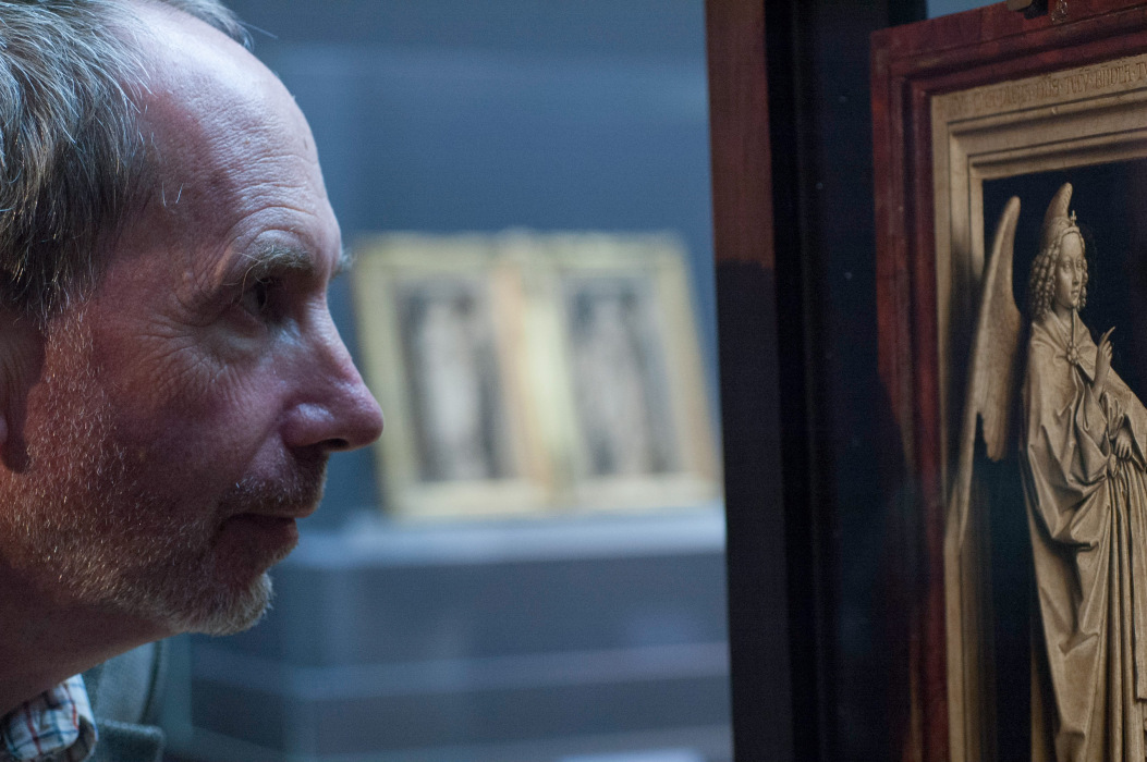 A photo of a man in profile, with grey hair and a short beard, looking deeply at a medieval work of an angel.