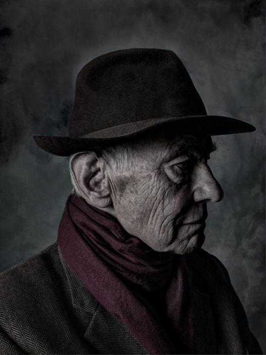 Darkly lit photograph of man with red scarf and brown fedora hat