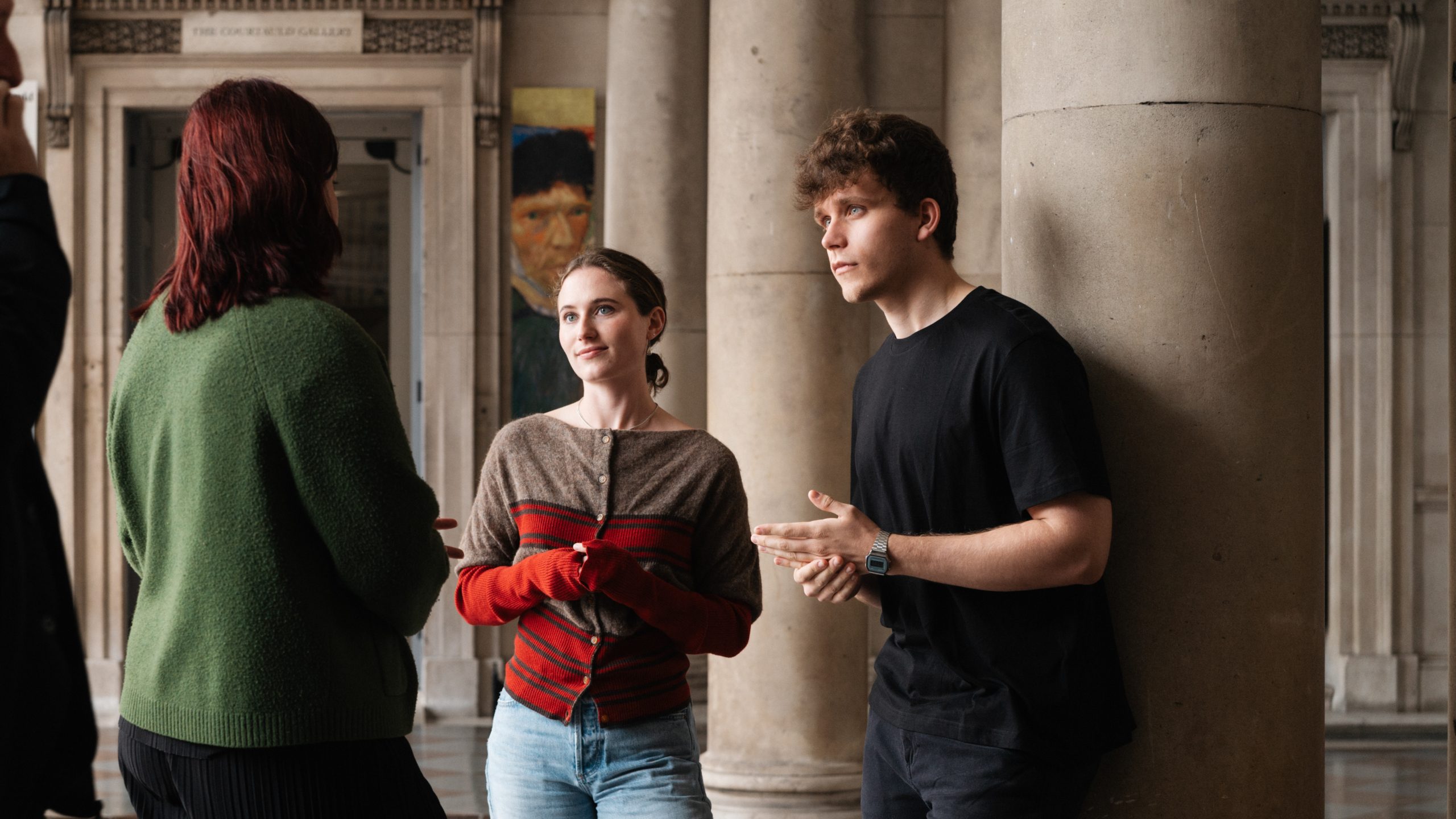 A group of three students gather under the Somerset house arches, the Courtauld Gallery in the background