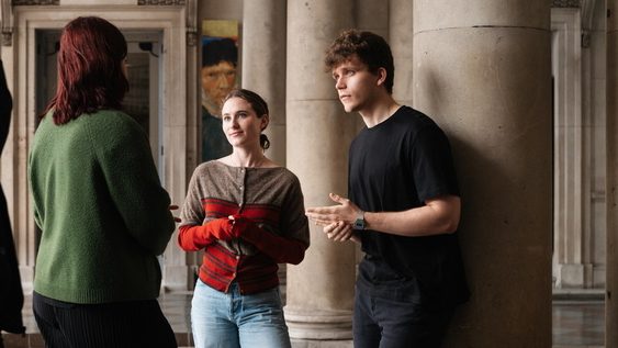 A group of three students gather under the Somerset house arches, the Courtauld Gallery in the background