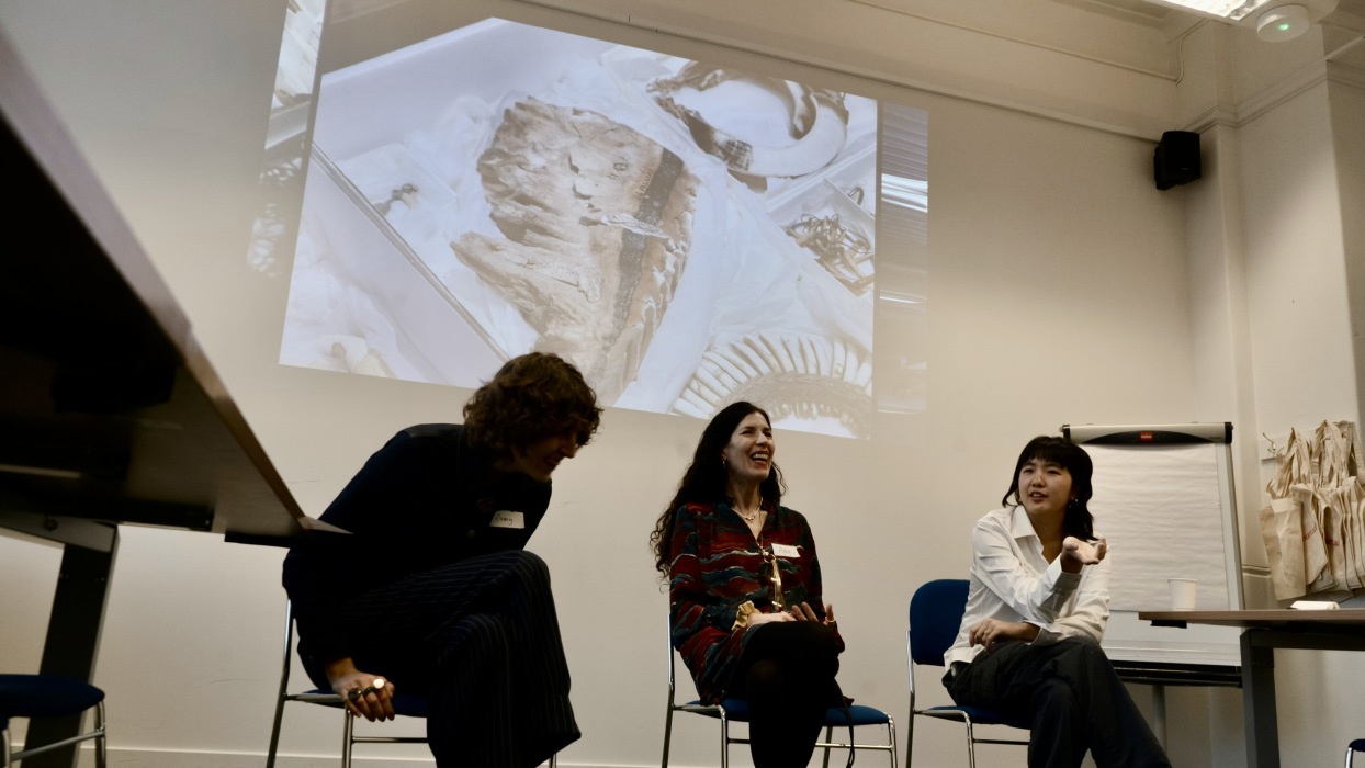 Three people sat in chairs, part of a panel with projection behind them