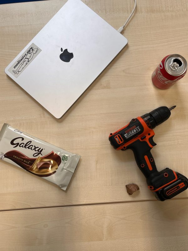 A laptop, a drill, a can of coke and a bar of chocolate on a table