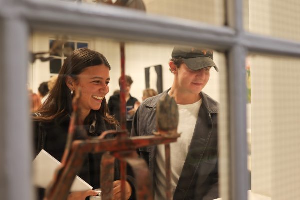 In the foreground, small abstract sculptures; in the background two smiling people view the artworks