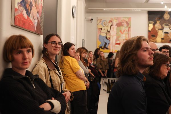A room of visitors leaning on wall, with paintings hanging above and behind them