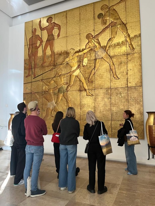 Viewers in a gallery stand in front of a large gold canvas