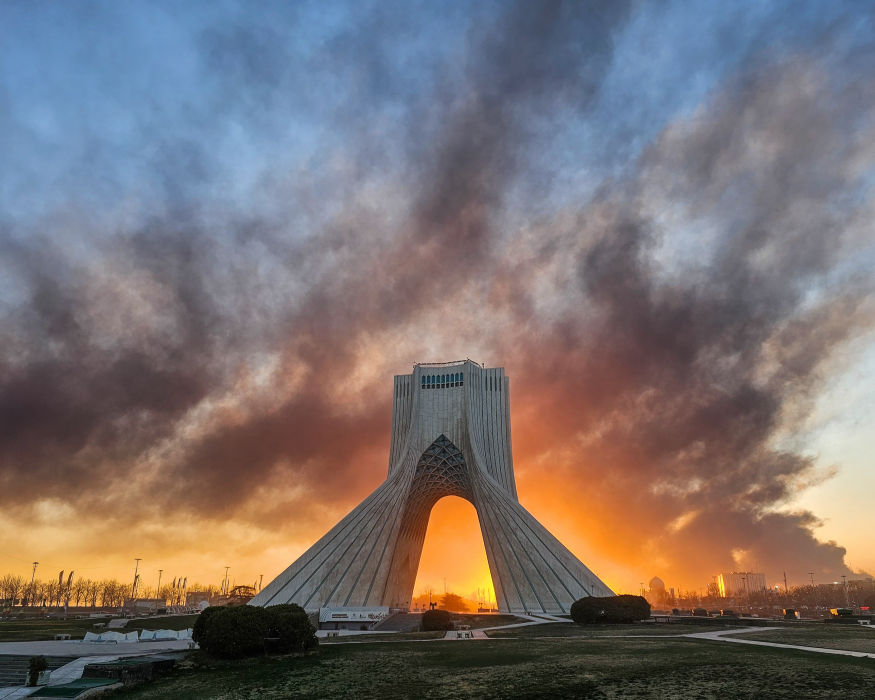 Tehran's Azadi Tower standing against a war torn sky,