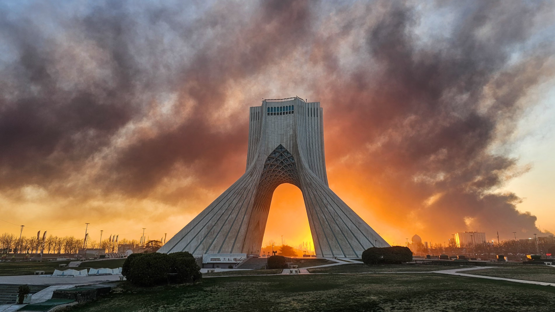 Tehran's Azadi Tower standing against a war torn sky,