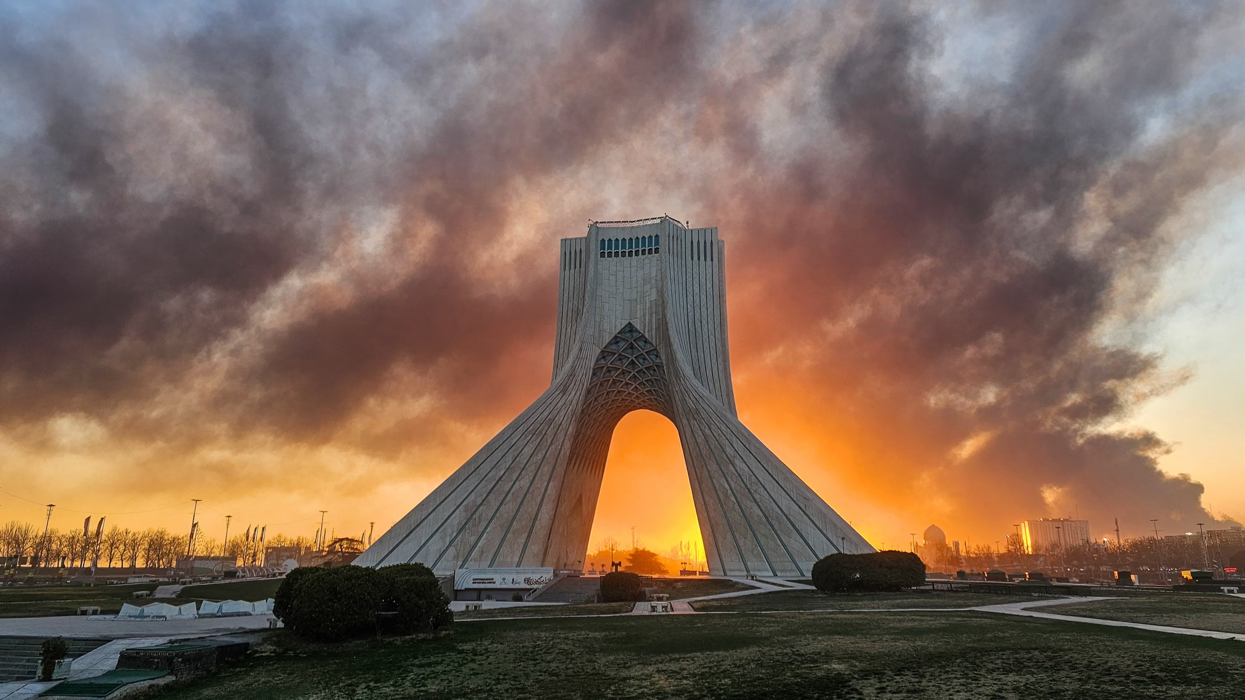 Tehran's Azadi Tower standing against a war torn sky,
