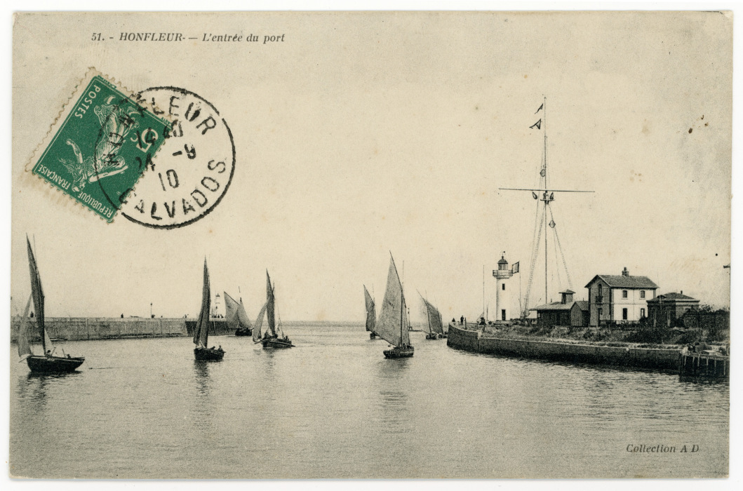 Black and white postcard of a port harbour with land and buildings on the right hand, and dominated by the open water with boats on the sea. Stamps visible in top left, and also text 'HONFLEUR - L'entree du port' above them.