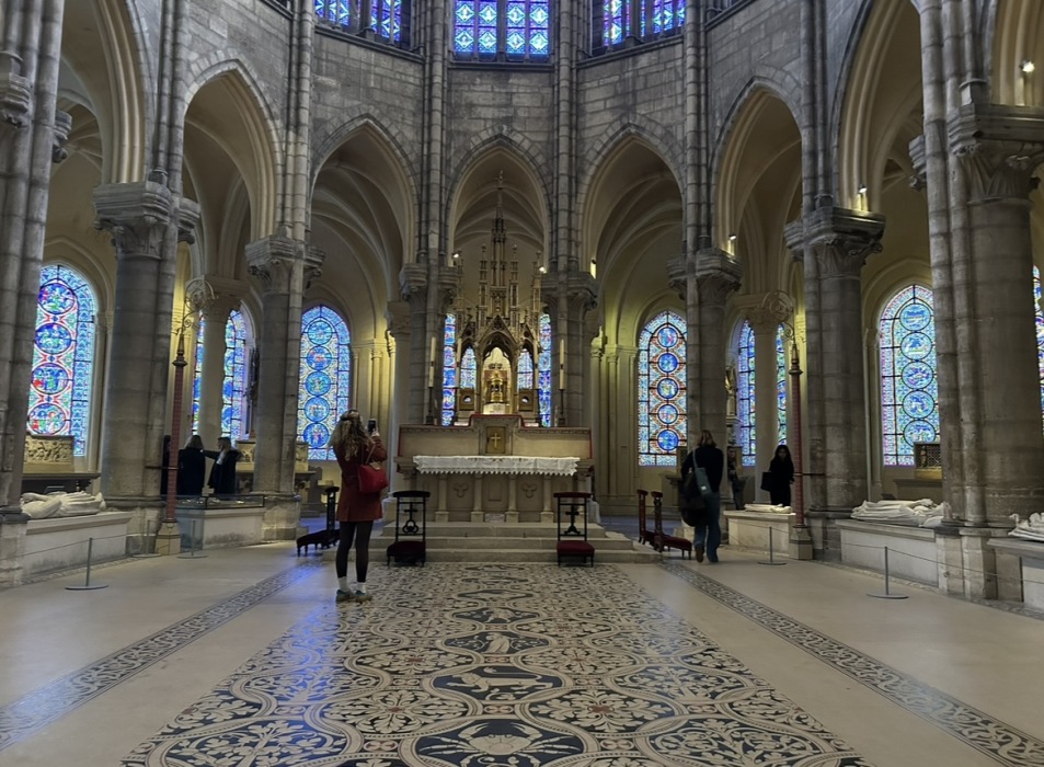 The knave of a church, with a blue tiled floor, stained glass, and an altar table.