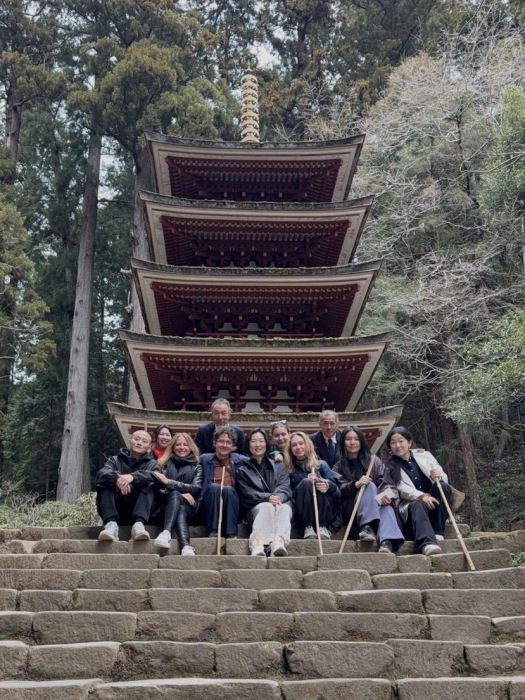 A group of people, young and old, sit in front of a Japanese building.