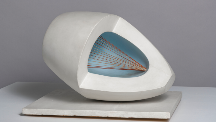 a wooden abstract sculpture featuring an oval form with pale blue and red painted surfaces, intersected by strings and mounted on a painted wooden base.
