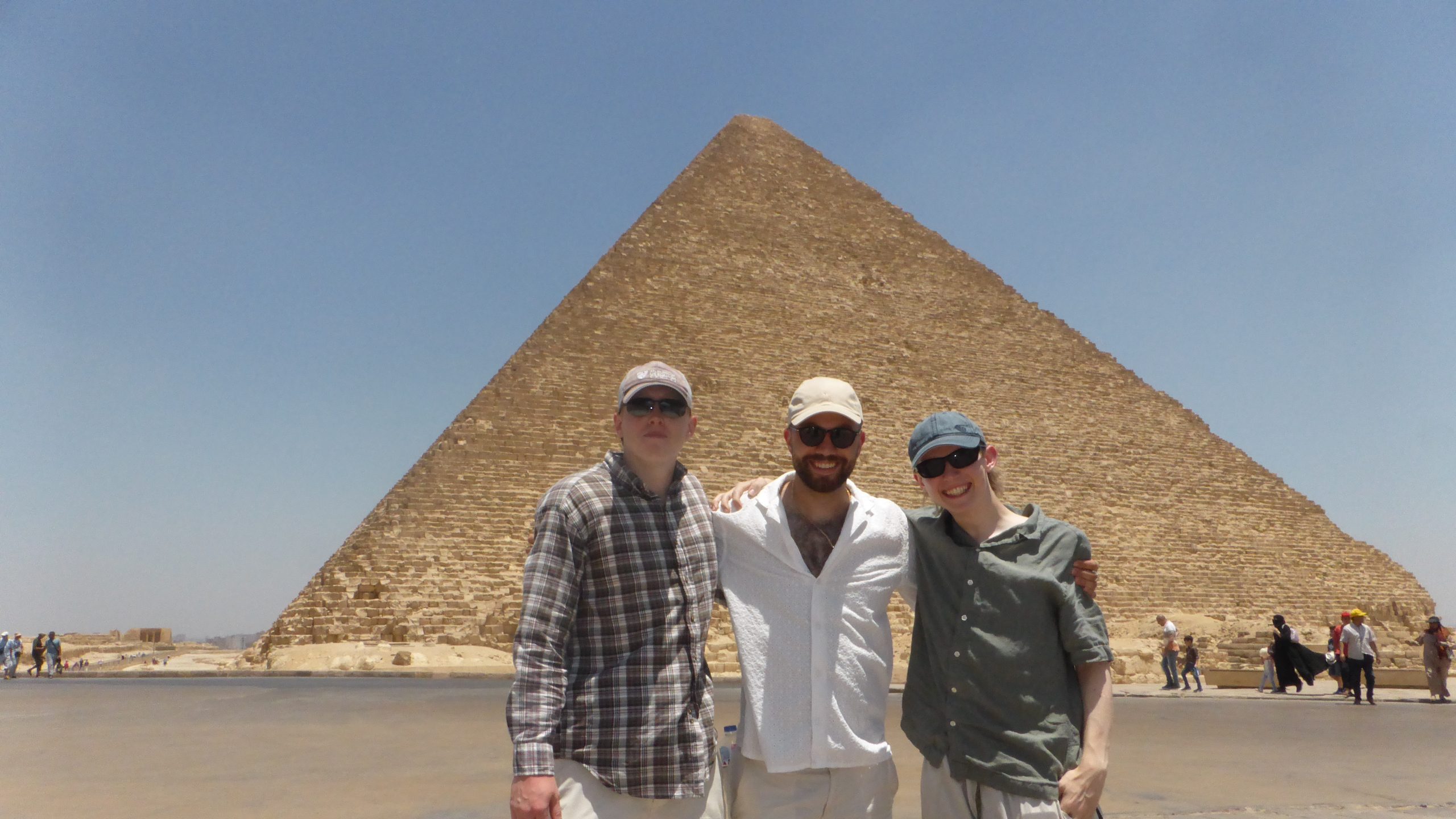 Three men in hats and sunglasses stand in front of a pyramid in Egypt.