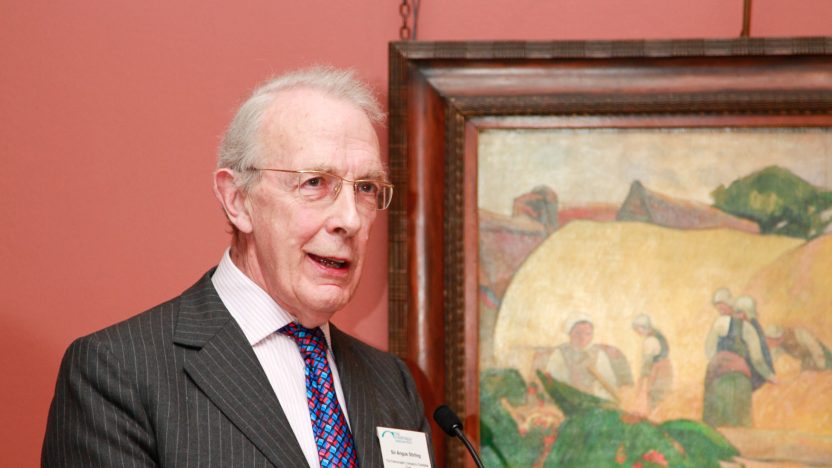 Angus Stirling standing in front of a framed Gauguin painting on a salmon-colour painted wall.