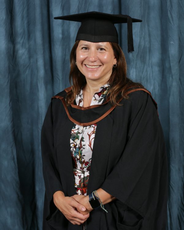 Louisa A Leventis smiling for an official photograph at the Courtauld, wearing black gown with a black and brown robes.