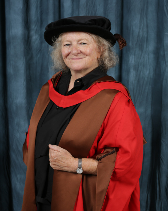 Rachel Whiteread smiling for an official graduation photo, dressed in a red gown with brown robes.