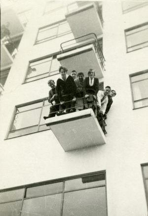A group of young people look down from a balcony