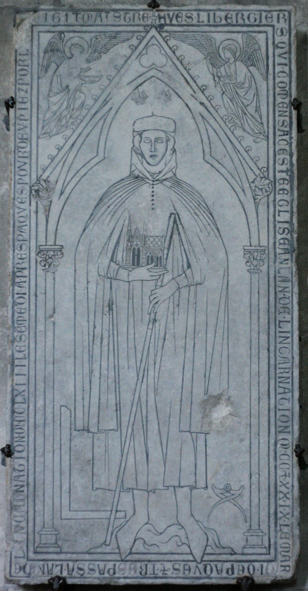 Chipped from age, engraved into stone, a depiction of a robed figure holding a small model of a cathedral in their hands. The figure seems to be standing in the cloisters of a gothic building. There are two angels above the figure's head, and Latin text wrapped around the depiction.