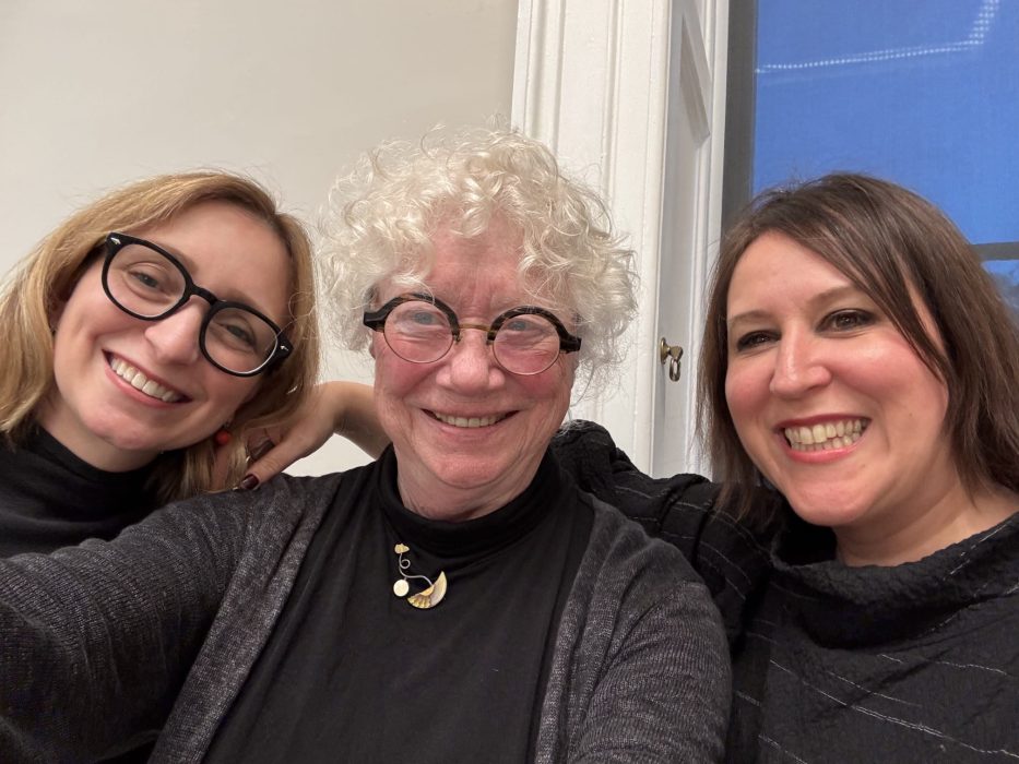 three white women of varying ages pose together smiling, all where black.