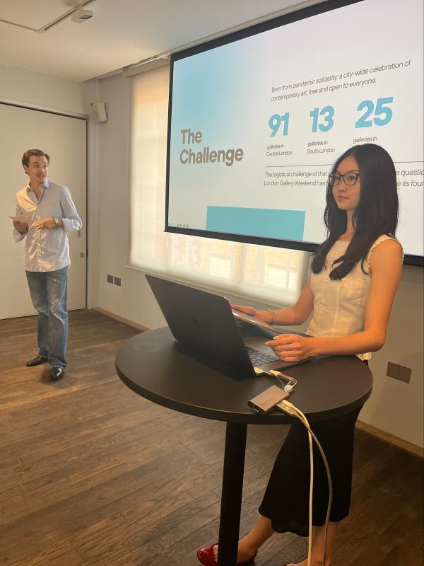 Two students, one standing in front of a laptop and the other in front of a projector. The slide identifies business challenges..