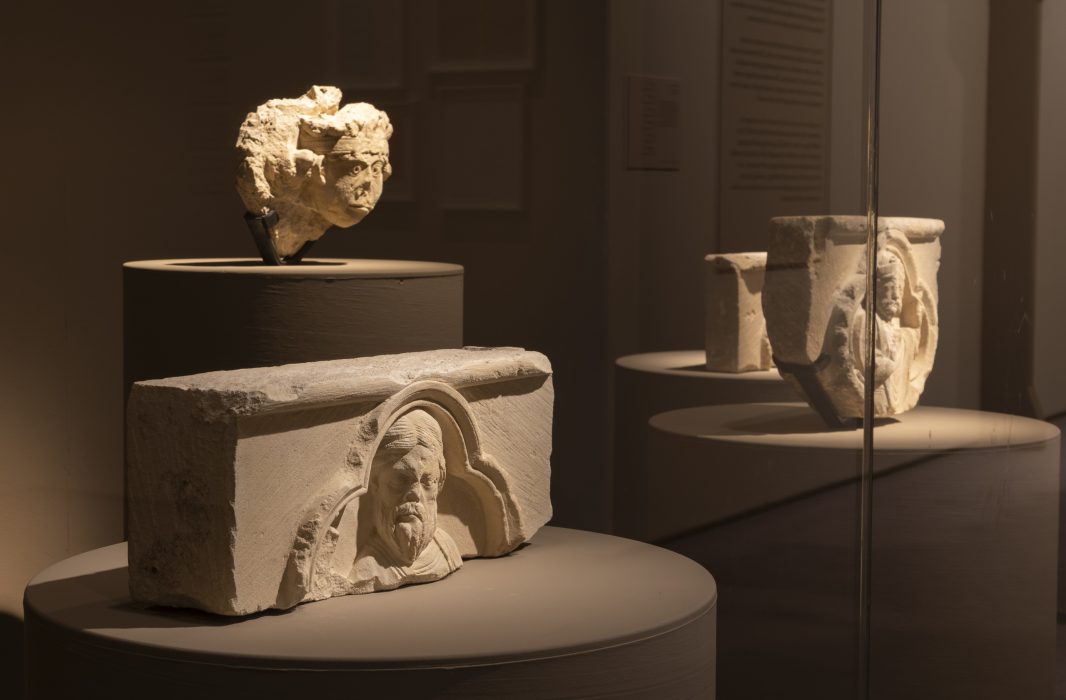 three ornate stone sculptures are spotlit against a dark room.