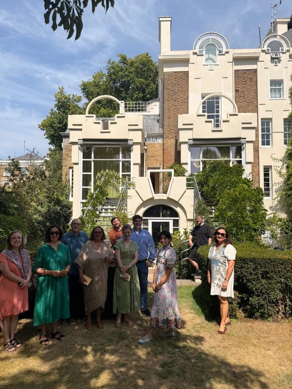 Members of the Interrogating Heritage research Cluster stand on the stairs leading into the garden of The Cosmic House