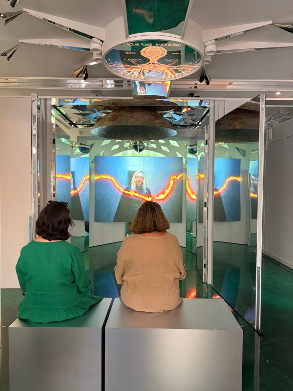 two figures sit and look a a video work at the Cosmic House