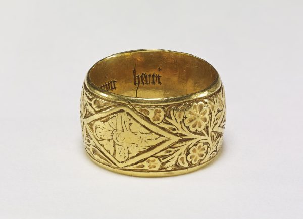 An ornate golden ring engraved with flowers. An icon in the centre seems to show a man and child, both haloed, though they are hard to make out as the engraving has faded over time. Latin text runs inside the ring.
