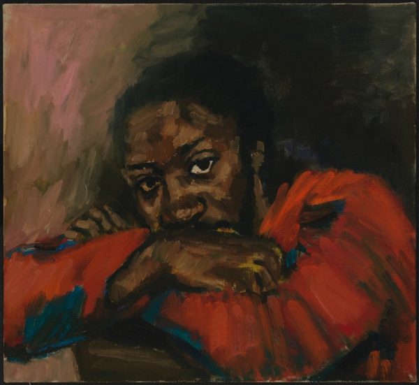 A portrait of a Black woman in a red jumper looks directly at the viewer. She has her face partially tucked into her arms. The background is shadowed and plain.