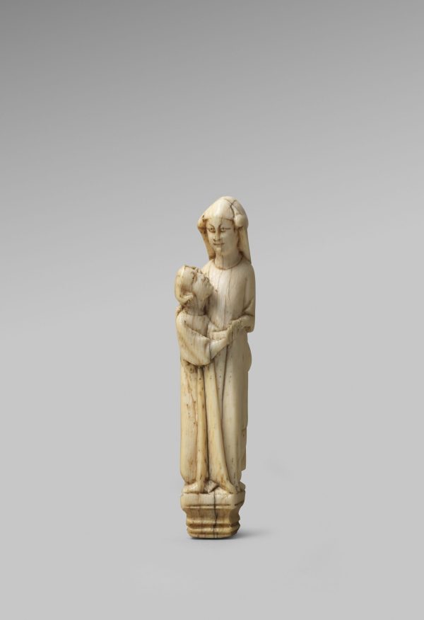 Carved out of a mottled white material, two figures stand on a plinth. One is taller, looks straight out, wearing a headdress. The other is shorter, looks up at the other figure. They are embracing.