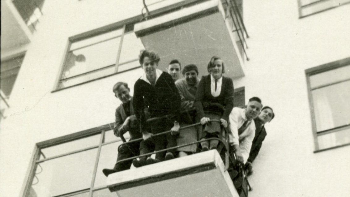 A group of young people look down from a balcony