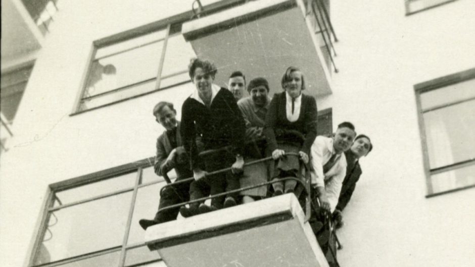 A group of young people look down from a balcony