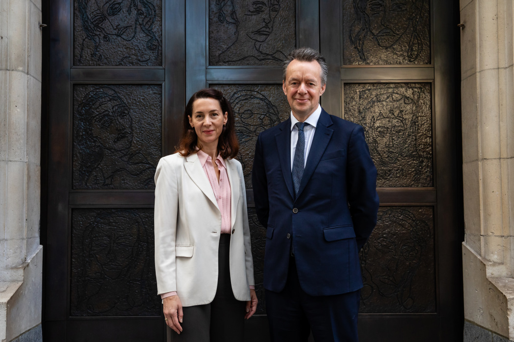 Two figures in suits stand in front of bronze doors
