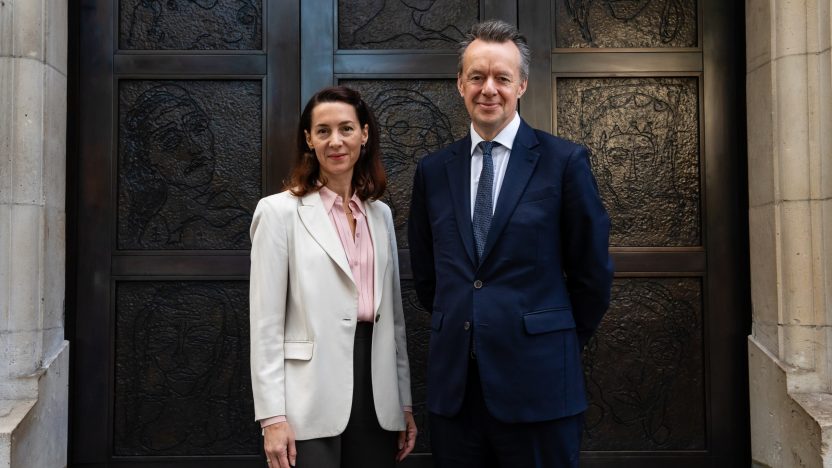 Two figures in suits stand in front of bronze doors