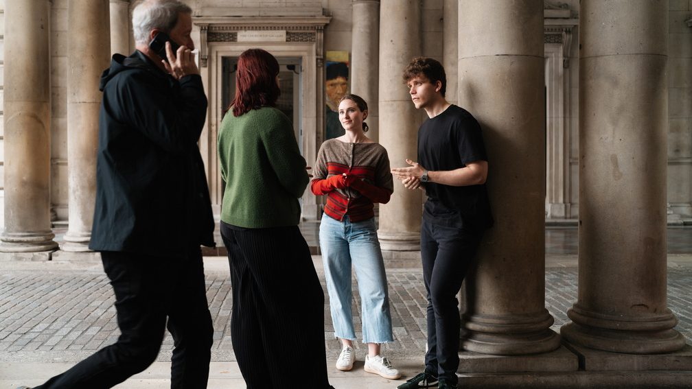 A group of three students gather under the Somerset house arches, the Courtauld Gallery in the background