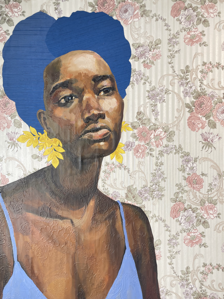 A portrait of a Black woman with large earrings like leaves and wearing a blue cami top. She has a pensive look on her face. She is against a floral wallpaper background; the pattern of the wallpaper is subtly in relief on her skin.
