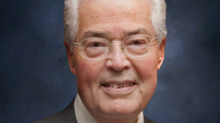 A man in a suit in front of a neutral background smiles at the camera