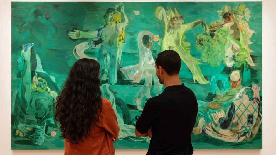 Two people stand in front of Salman Toor's large scale painting, Ghost Ball