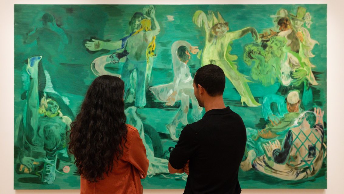 Two people stand in front of Salman Toor's large scale painting, Ghost Ball